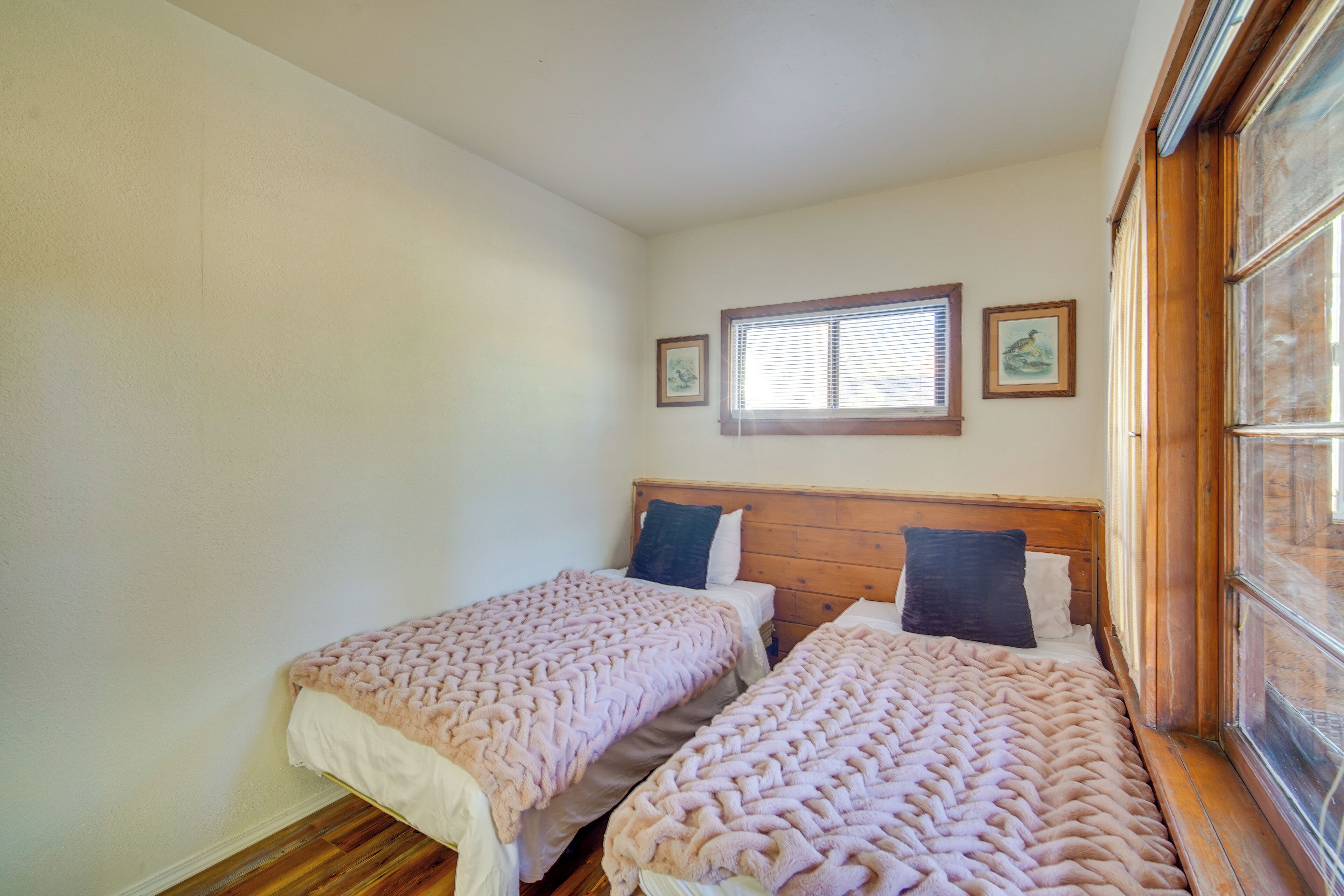 Ein Schlafzimmer mit zwei Einzelbetten, hölzernen Kopfteilen, einem Fenster mit Jalousien und gerahmten Bildern an der Wand.