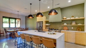 Une cuisine moderne dotée d’un îlot central, de tabourets de bar, de luminaires suspendus et de meubles de rangement en bois.