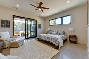 A spacious bedroom with a large bed, a ceiling fan, a sliding glass door leading to a balcony, and a view of the outdoors.