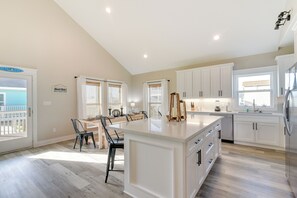A spacious kitchen with a large island, white cabinetry, and a view of the ocean through the windows. - Galveston Home w/ Pool Access, Walk to Beaches! (Galveston)