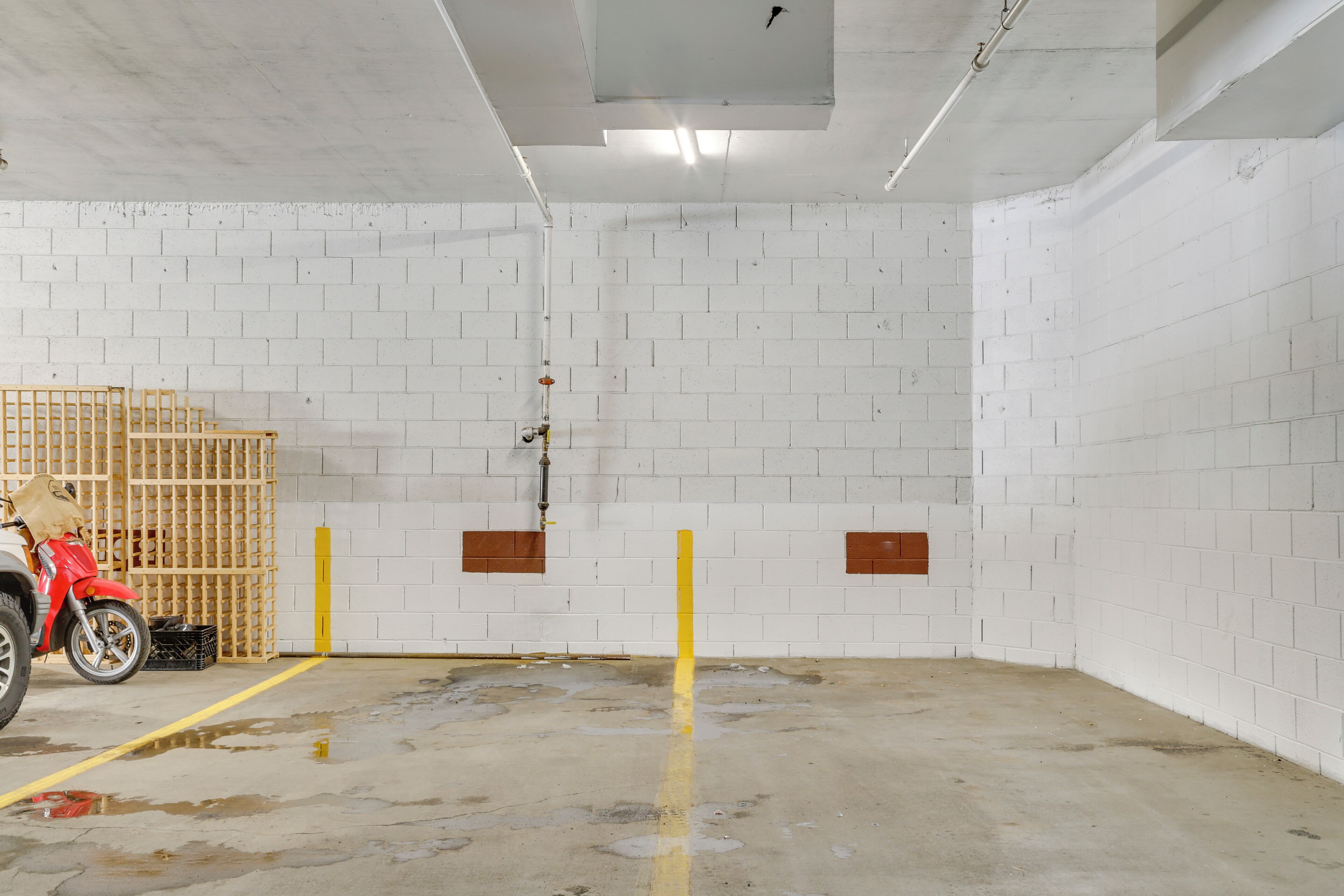 A clean, white-walled room with a concrete floor, a yellow line marking, and a red motorcycle.