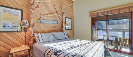 A cozy cabin-style bedroom with a bed, a nightstand, and a window with a view of the snowy outdoors.