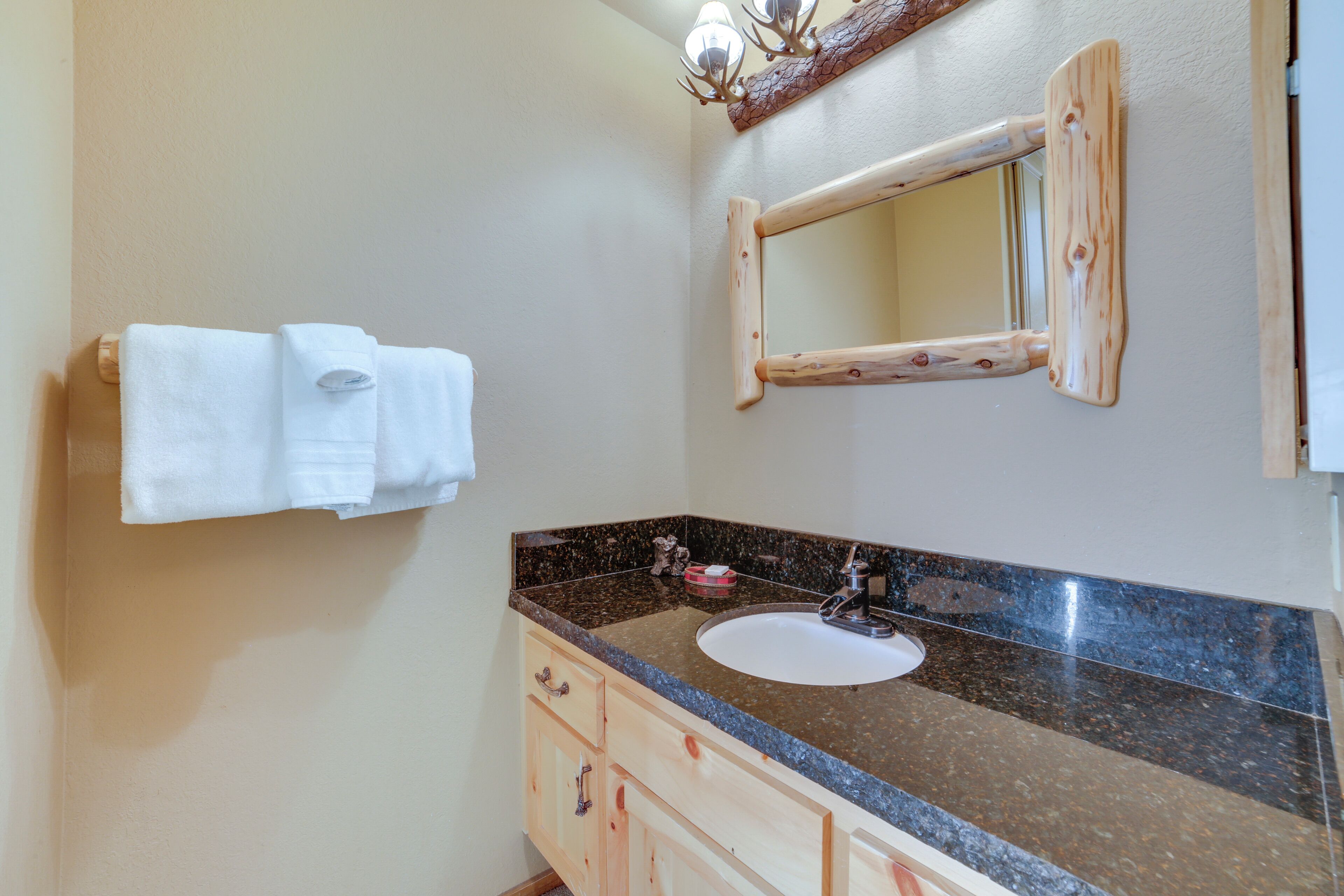 A bathroom with a granite countertop, a sink, wooden cabinets, and a mirror with a wooden frame.
