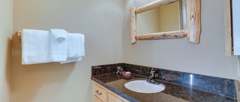 A bathroom with a granite countertop, a sink, wooden cabinets, and a mirror with a wooden frame.