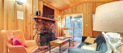 A wooden interior with a fireplace, leather armchair, sofa, and a dining table.
