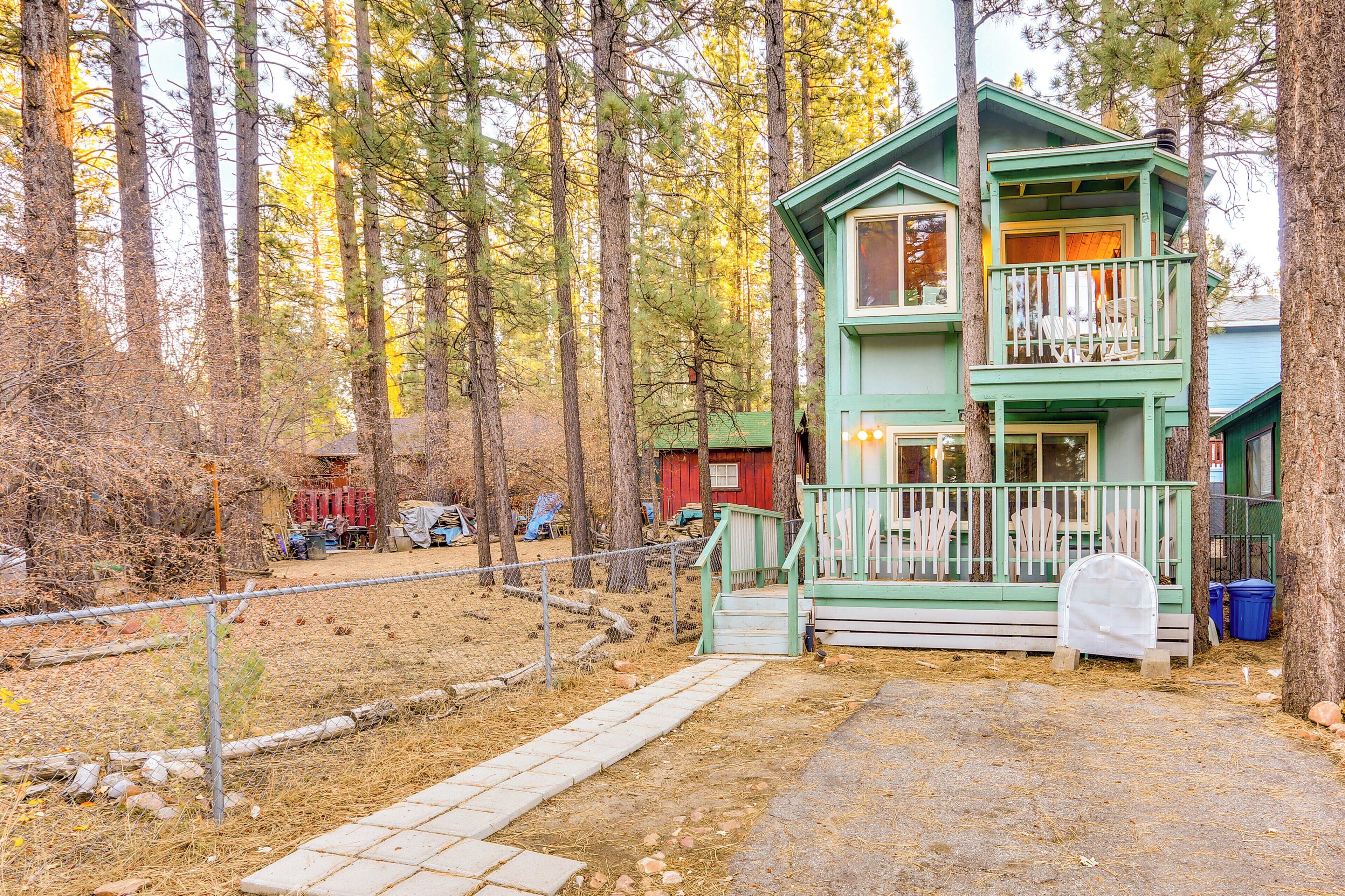 A two-story cabin with a balcony, surrounded by a forest.