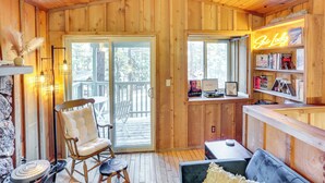 Tunnelmallinen, puinen mökki, jossa on liukuovi, joka johtaa ulkoterasille. Sisätiloissa on mukava oleskelualue ja neonvalomainos, jossa lukee: ”Ski Lodge”.