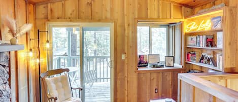 Een gezellig houten chalet interieur met een schuifdeur naar een terras, een comfortabele zithoek en een neonbord waarop staat