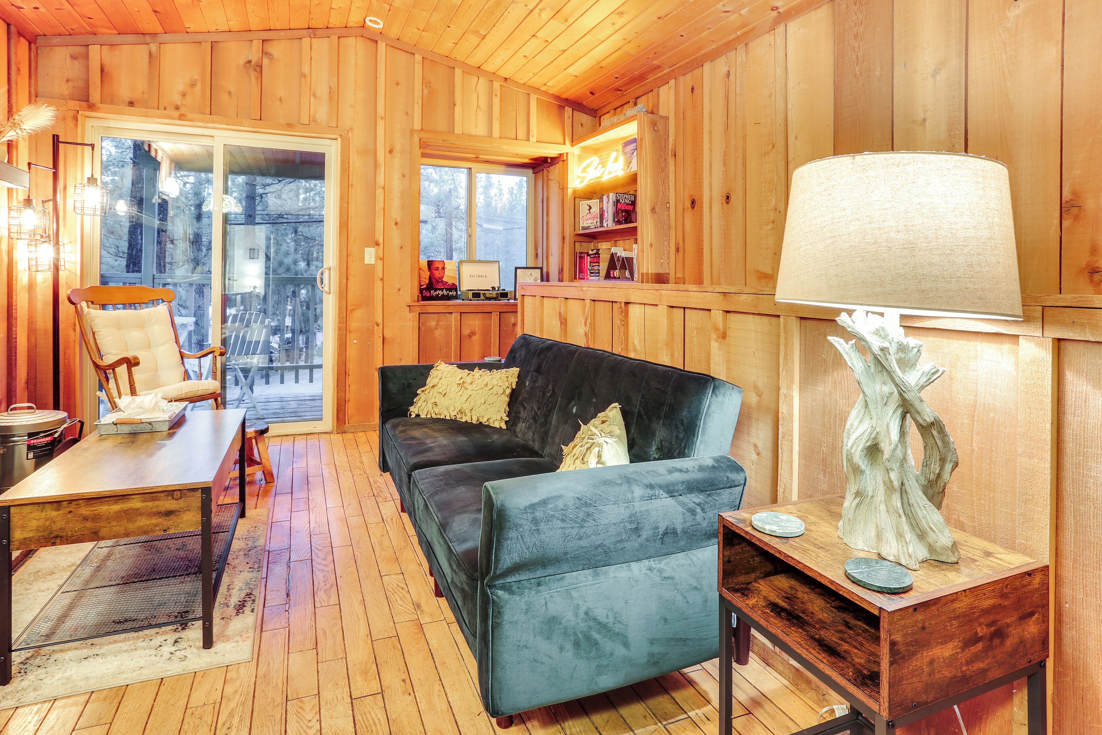 Interior acogedor de una cabaña con detalles de madera, un sofá negro, una mesa de madera y una lámpara.