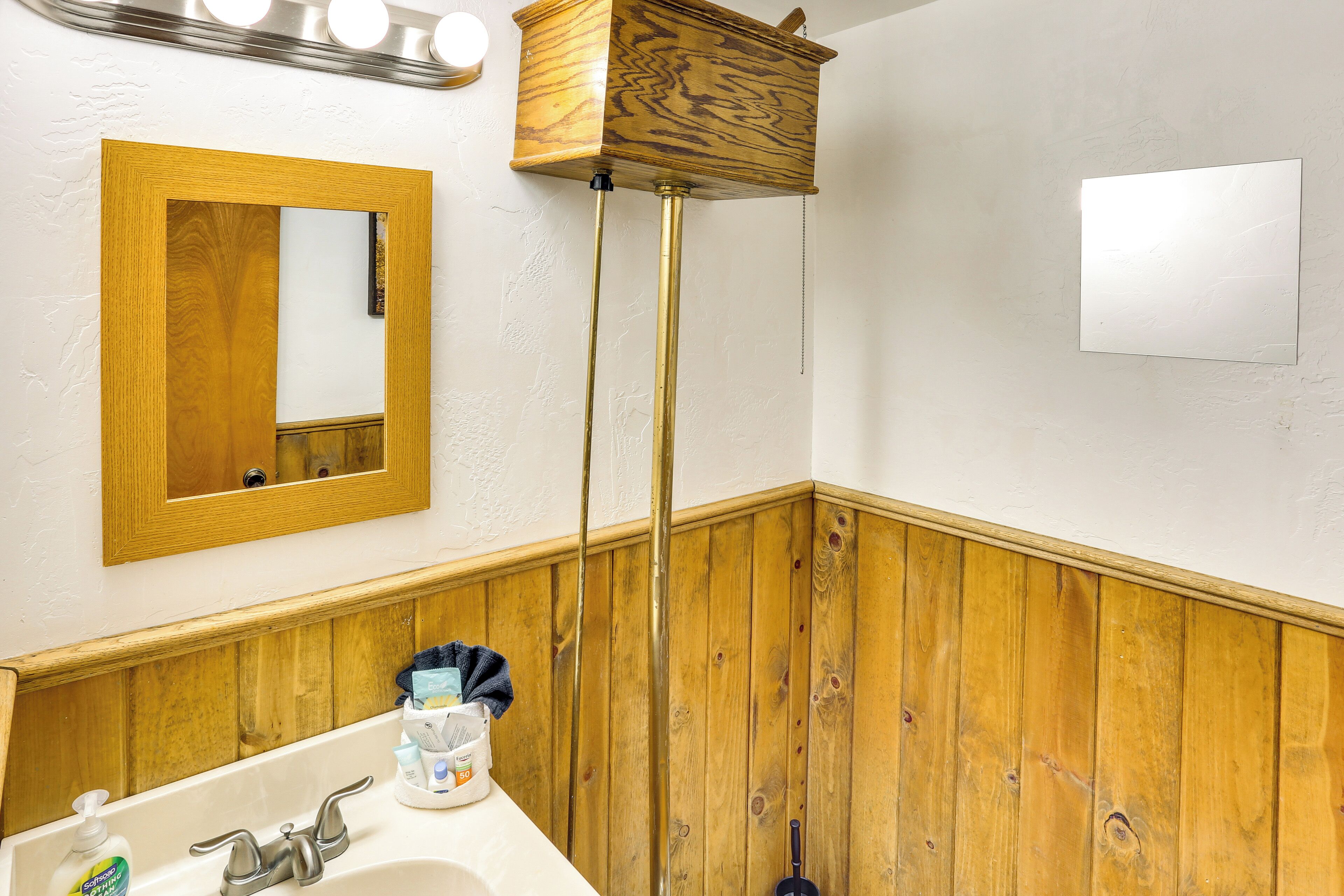 Une salle de bain avec un meuble-lavabo en bois, un miroir, un lavabo avec des articles de toilette et un lambris en bois.