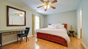 A bedroom with a wooden bed, a desk, a chair, a ceiling fan, and a mirror.