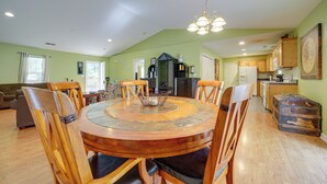 A spacious dining area with a round wooden table surrounded by chairs, a chandelier, and a kitchen in the background.