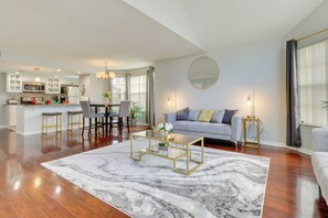 A spacious living area with a marble-patterned rug, a sofa, and a coffee table. A kitchen with modern appliances and bar stools is visible in the background. - Kissimmee Condo w/ Perks: 6 Mi to Disney World! (Kissimmee)