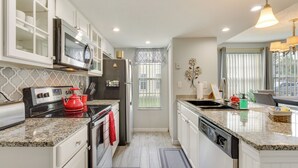 A modern kitchen with white cabinetry, granite countertops, stainless steel appliances, and a window with a view. - Kissimmee Condo w/ Perks: 6 Mi to Disney World! (Kissimmee)