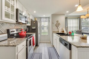 A modern kitchen with white cabinets, granite countertops, stainless steel appliances, and a window with a view. - Kissimmee Condo w/ Perks: 6 Mi to Disney World! (Kissimmee)