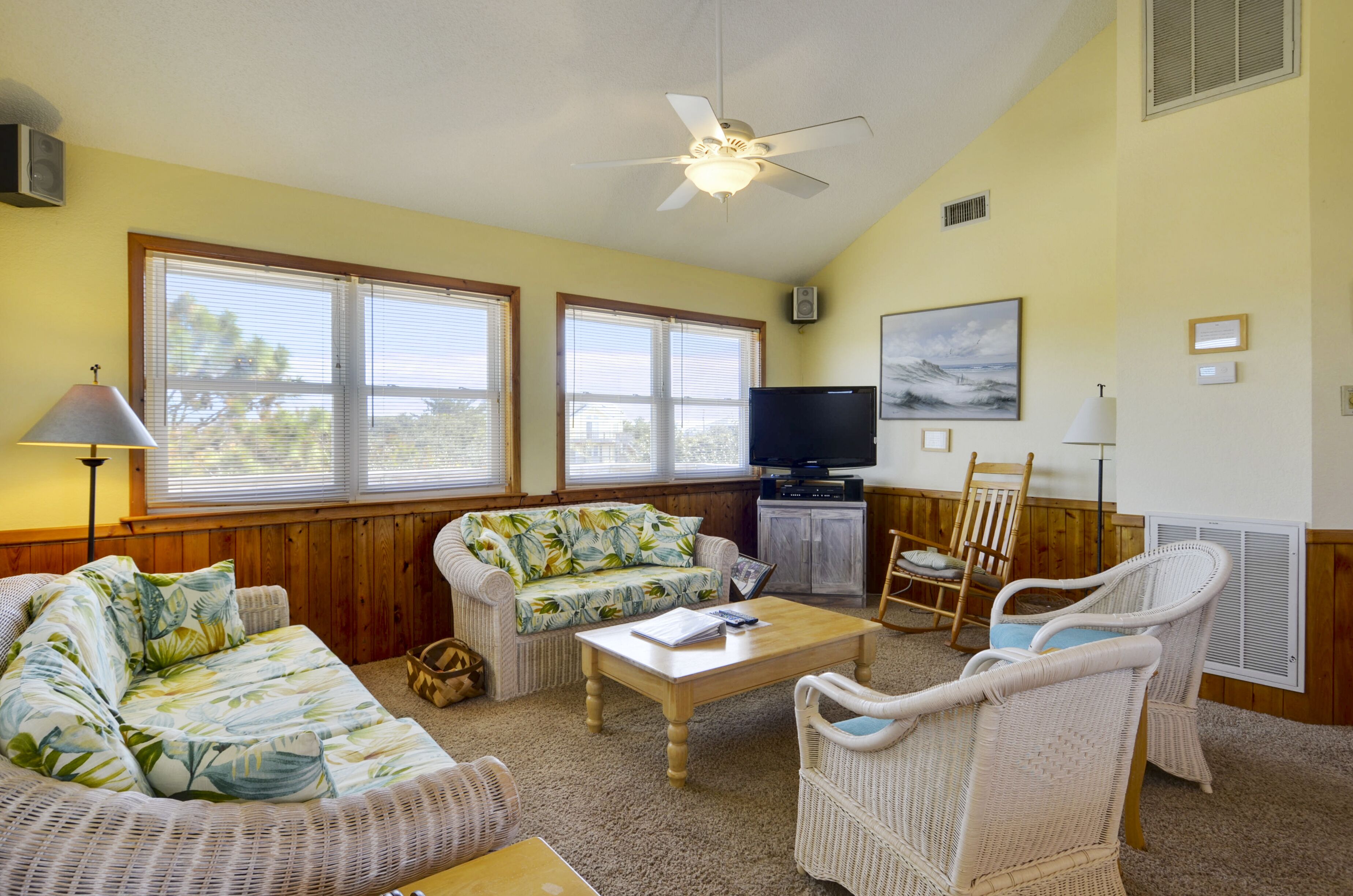 A living room with a sofa, chairs, a coffee table, a television, and large windows.