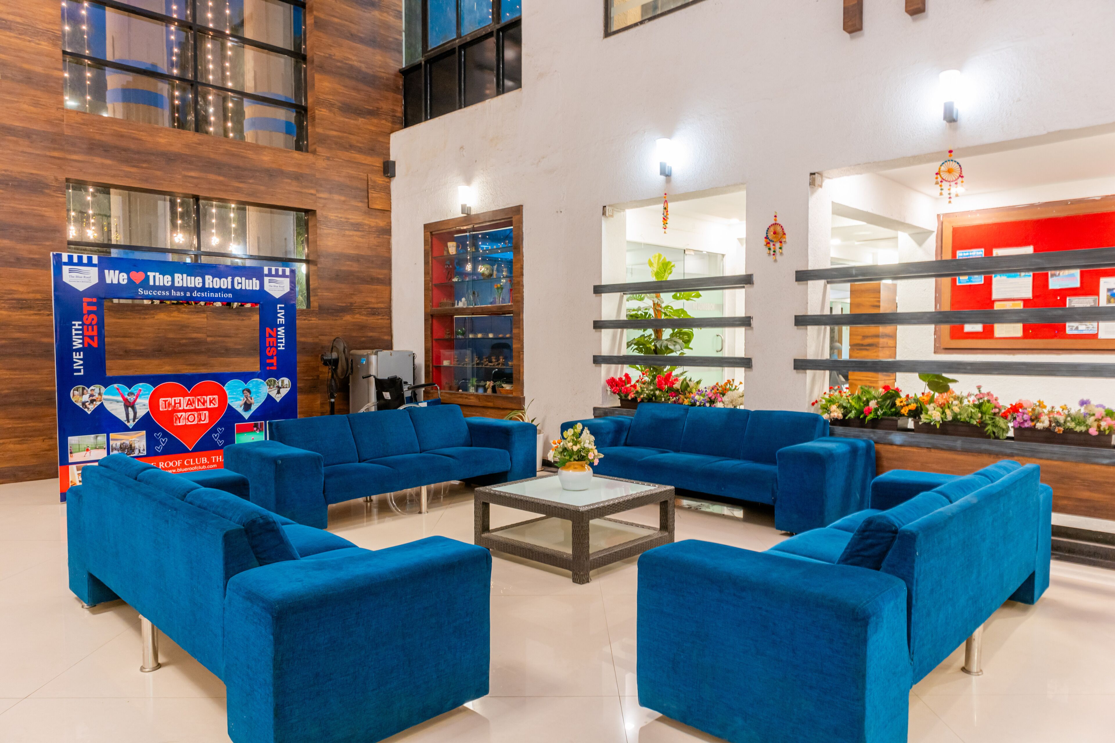 Um hall moderno com sofás azuis, uma mesa de centro de vidro e uma receção com fundo vermelho.