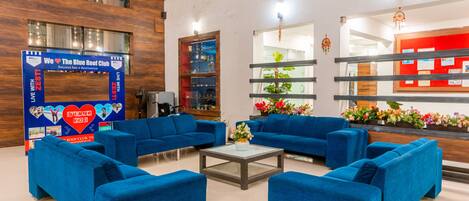 Um hall moderno com sofás azuis, uma mesa de centro de vidro e uma receção com fundo vermelho.