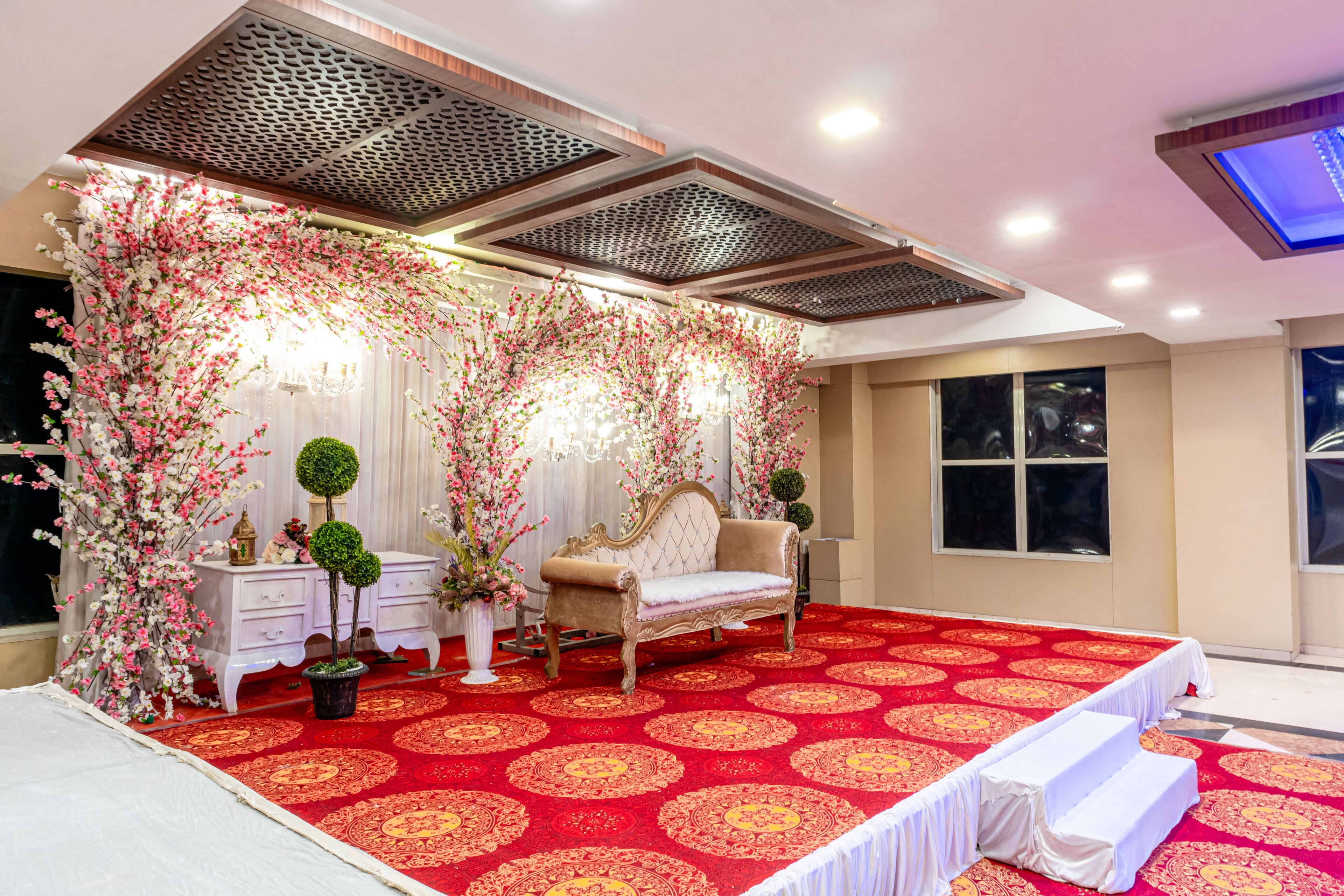 A room with a red carpet, a white sofa, and decorative floral arrangements.