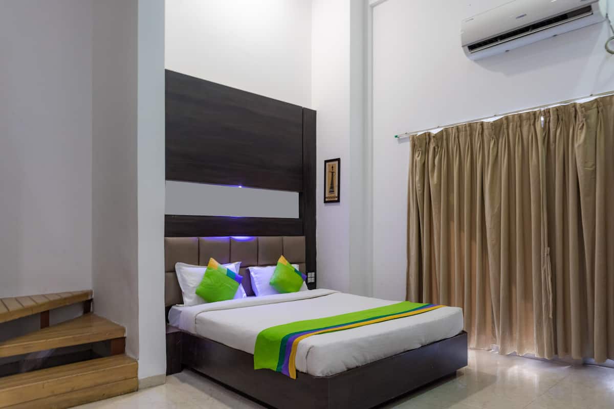 A bedroom with a bed, a headboard, a window with curtains, a staircase, and an air conditioning unit.