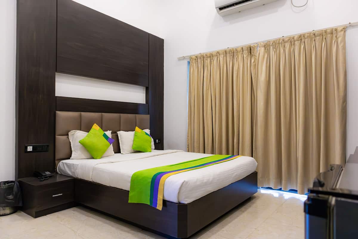 A modern hotel room with a large bed, a dark wood headboard, a beige curtain, and a small bedside table with a phone.