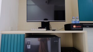 A flat-screen TV mounted on a wooden wall, a minibar with a minibar machine, and a refrigerator below.