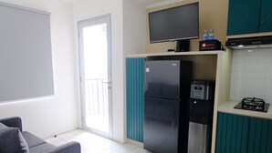 A compact kitchen with a refrigerator, a flat-screen TV, and a water dispenser.