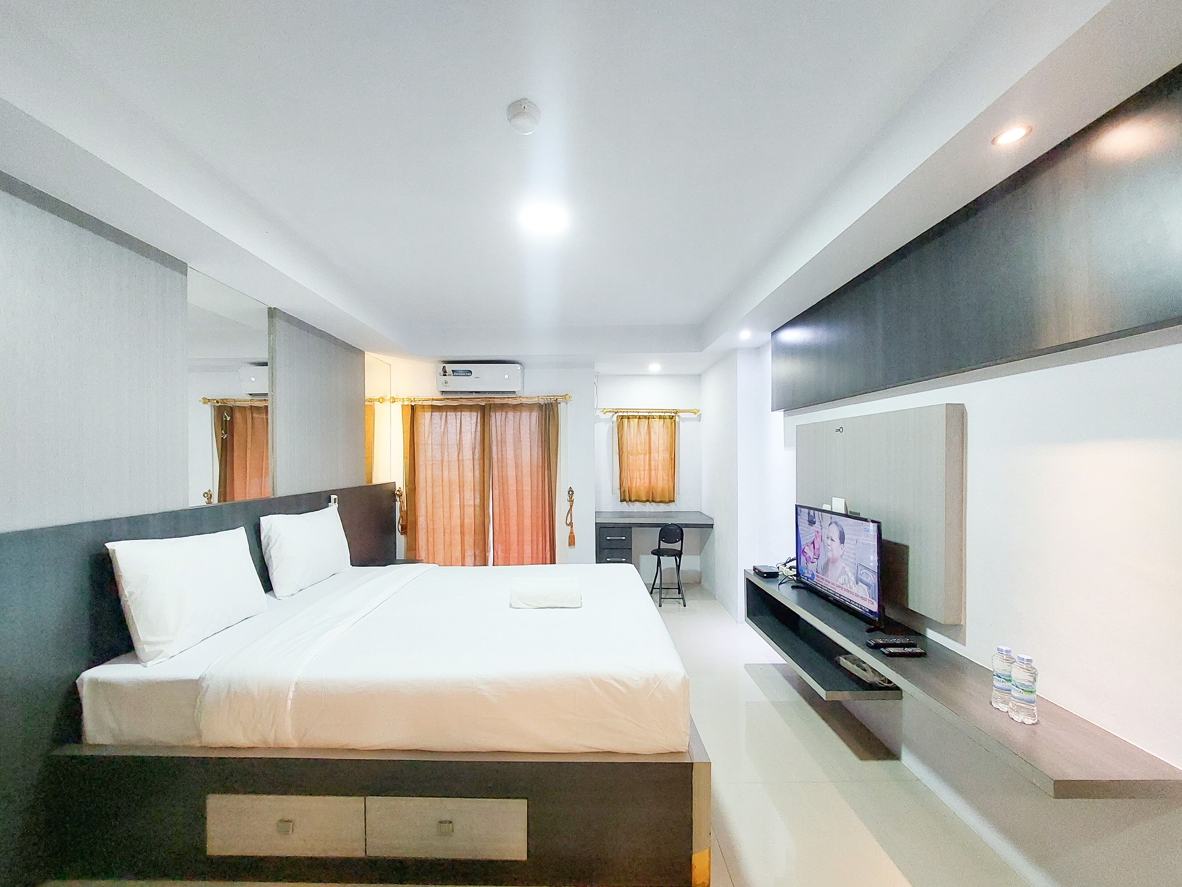 A modern hotel room with a large bed, a desk, a TV, and a mirror.