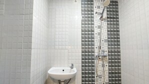 Een badkamer met een witte wastafel, een douche met een behangwand en een betegelde vloer.
