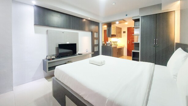 Een moderne hotelkamer met een groot bed, een televisie, een bureau met computer en een kitchenette.