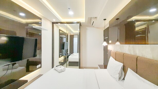 A modern hotel room with a large bed, a flat-screen TV, a mirror, and a ceiling light fixture. - Spacious And Elegant 1Br At Patraland Amarta Apartment (Ngaglik)