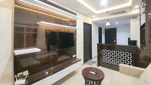 A modern living room with a large flat-screen TV, a sofa, a coffee table, and a patterned wall. - Spacious And Elegant 1Br At Patraland Amarta Apartment (Ngaglik)