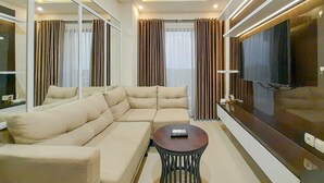 A modern living room with a sectional sofa, a round coffee table, and a large flat-screen TV. - Spacious And Elegant 1Br At Patraland Amarta Apartment (Ngaglik)