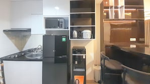 A compact kitchen with a refrigerator, microwave, and a coffee machine. There is a small sink and a chair near the counter. - Spacious And Elegant 1Br At Patraland Amarta Apartment (Ngaglik)