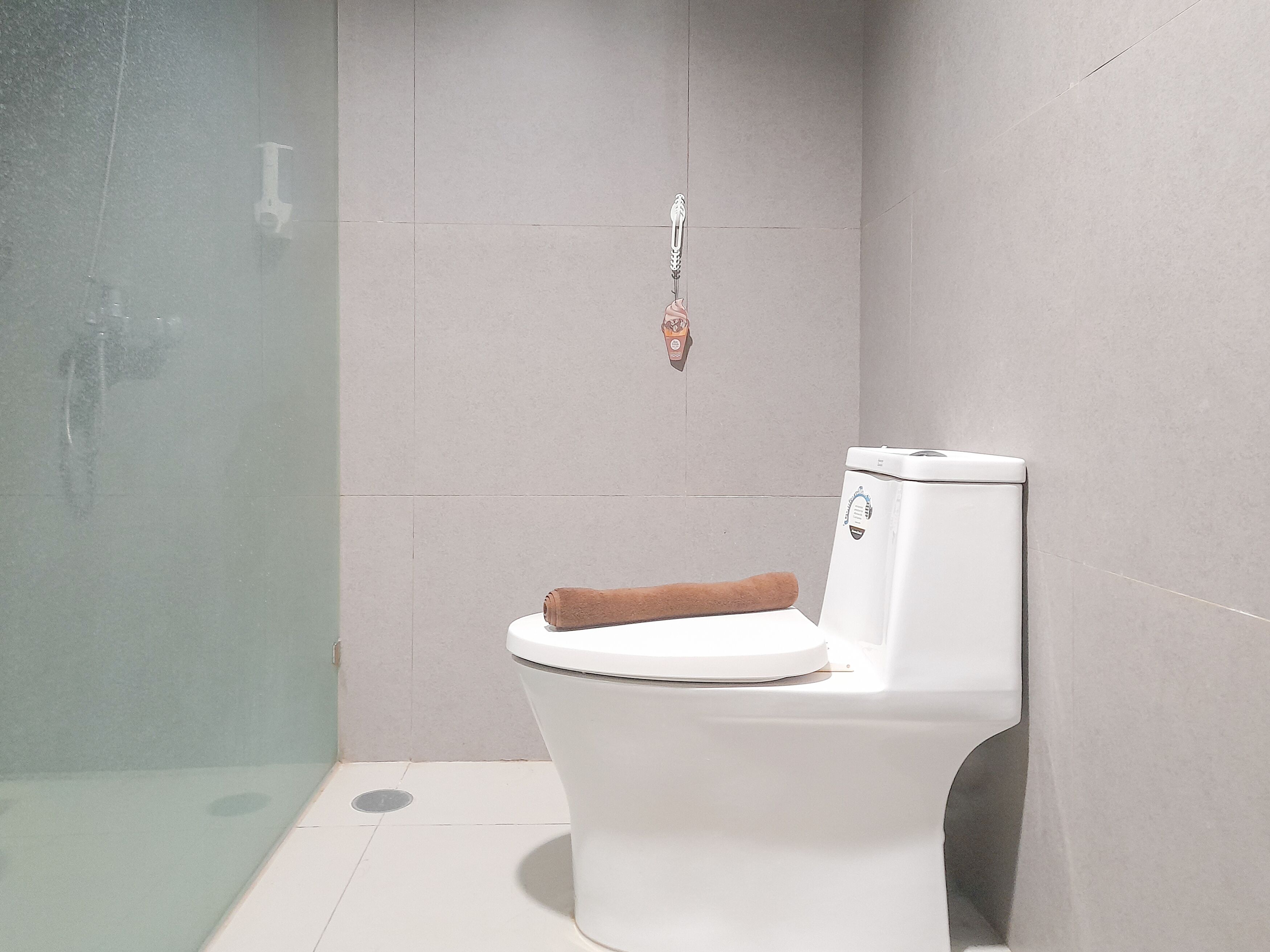 A bathroom with a white toilet, a towel on the seat, and a shower area with a glass door.
