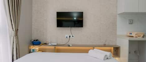 Camera d'albergo con un letto, una TV a muro, un comodino con una lampada e un bagno con un portascopevoli.