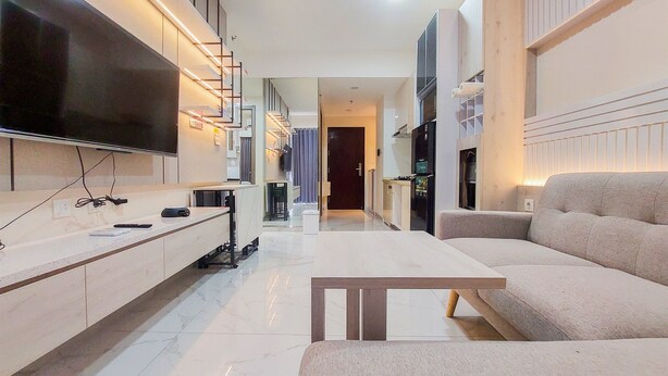 A modern living room with a flat-screen TV, a sofa, a coffee table, and a kitchen area in the background. - Elegant And Strategic 2Br Sky House Bsd Apartment Near Ice Bsd (Pagedangan)