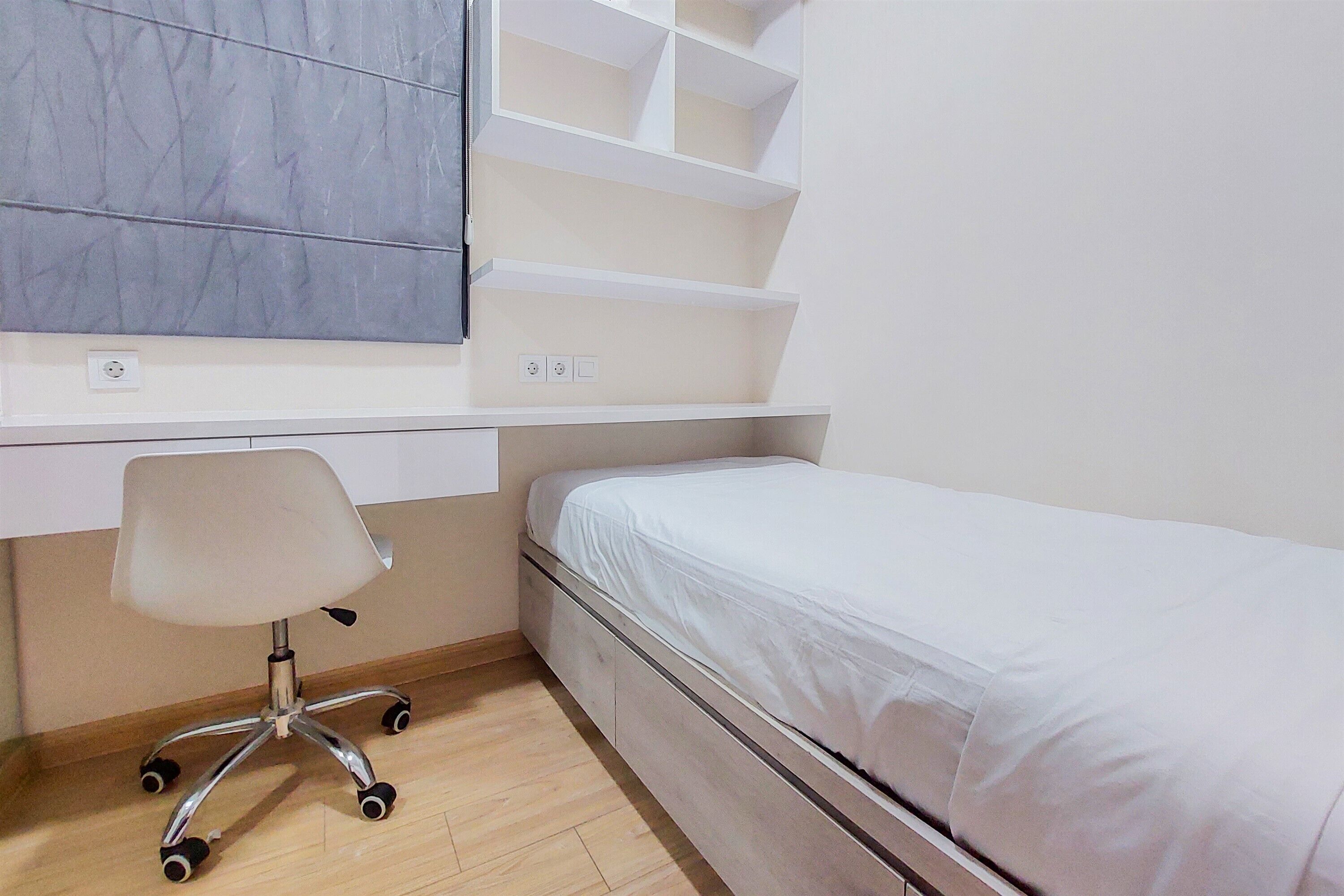 Ein Schlafzimmer mit Bett, Schreibtisch mit Stuhl und integrierten Regalen.
