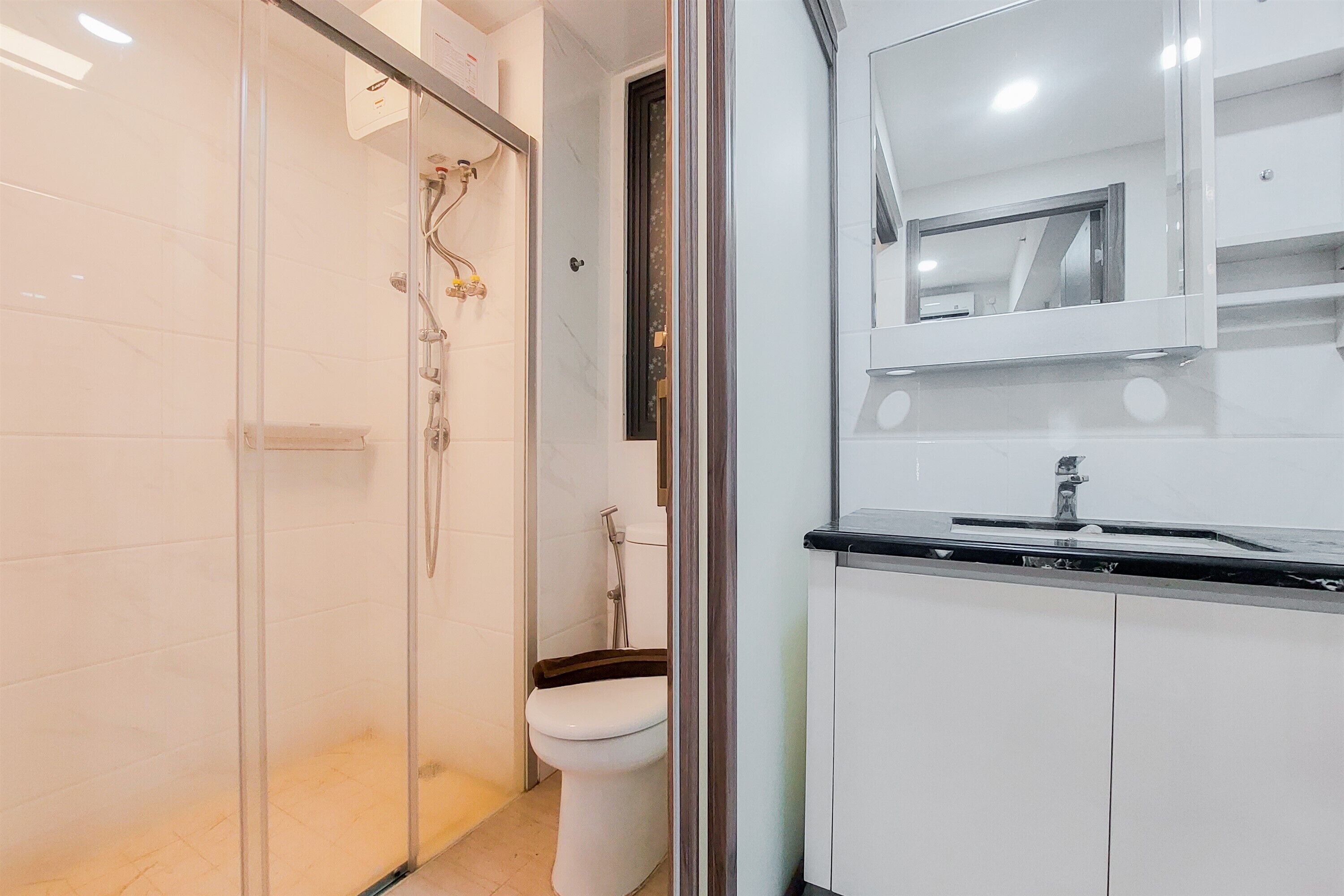 Un baño moderno con cabina de ducha de vidrio, inodoro blanco y lavabo con espejo arriba.