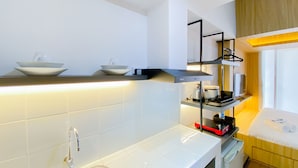 A compact kitchen with white tiles, a stainless steel sink, and a compact refrigerator.