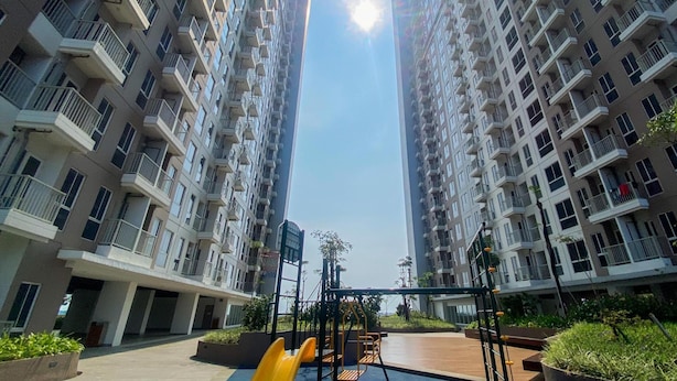 A high-rise residential building with multiple balconies, a playground area with slides, and a clear sky.