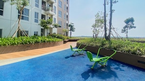 A rooftop pool area with exercise equipment, surrounded by greenery and a modern building.