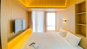 A modern hotel room with a large bed, a flat-screen TV mounted on the wall, and a bedside table with a remote control and towels.