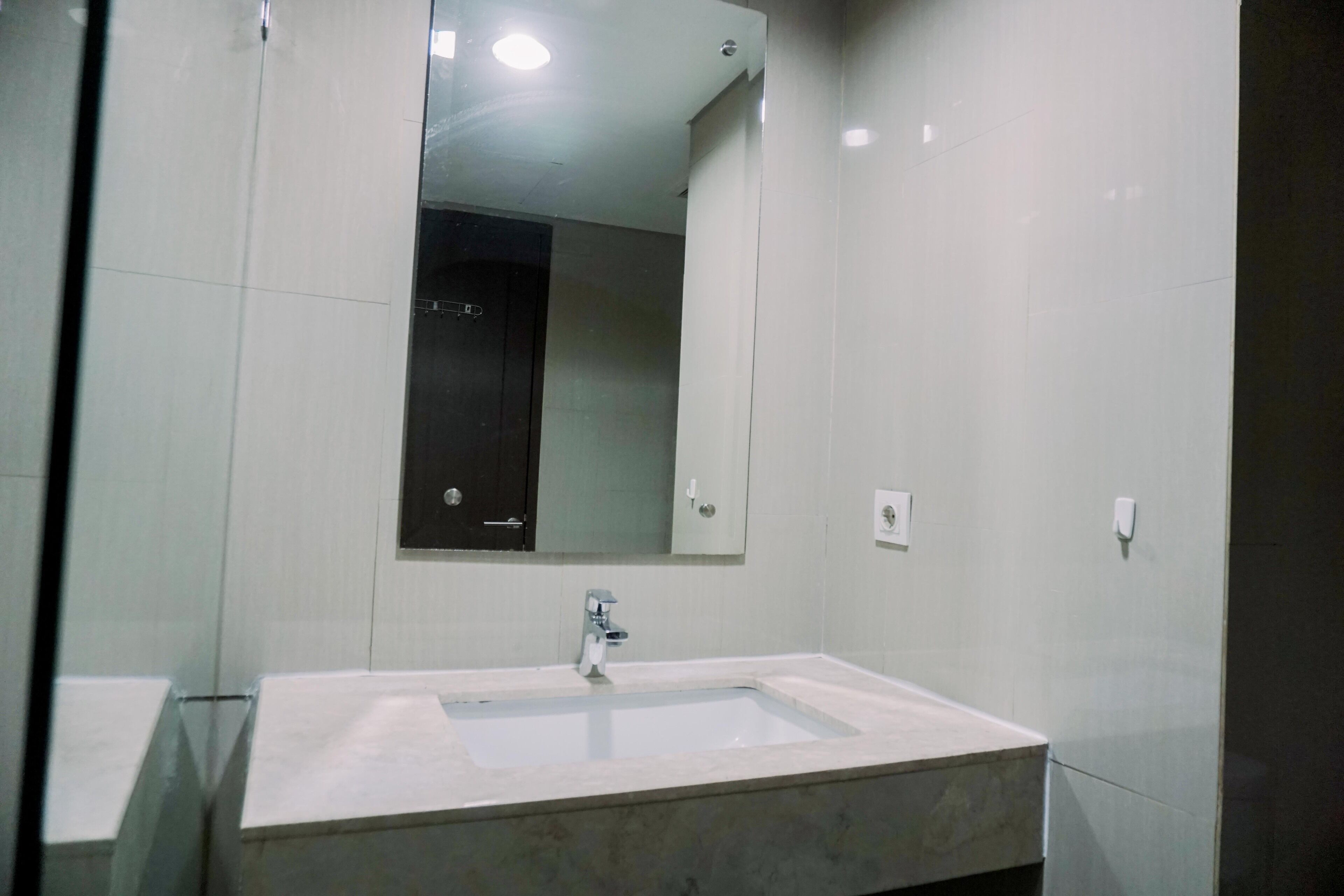 Ein Badezimmer mit einem rechteckigen Waschbecken, einem Spiegel darüber und einer dunklen Tür im Hintergrund.