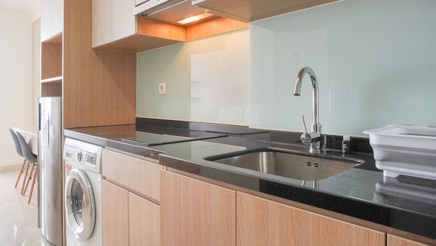 A modern kitchen with a stainless steel sink, a built-in washing machine, and wooden cabinetry. - Warm And Best Studio At Menteng Park Apartment (Jakarta)