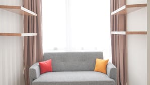 A grey sofa with red and yellow pillows, positioned between two curtains and a window. - Warm And Best Studio At Menteng Park Apartment (Jakarta)