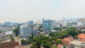 A cityscape with modern buildings, including a distinctive curved glass structure, surrounded by greenery and traditional architecture. - Warm And Best Studio At Menteng Park Apartment (Jakarta)