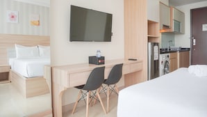 A hotel room with a bed, a desk with two chairs, a TV, a washing machine, and a kitchenette. - Warm And Best Studio At Menteng Park Apartment (Jakarta)