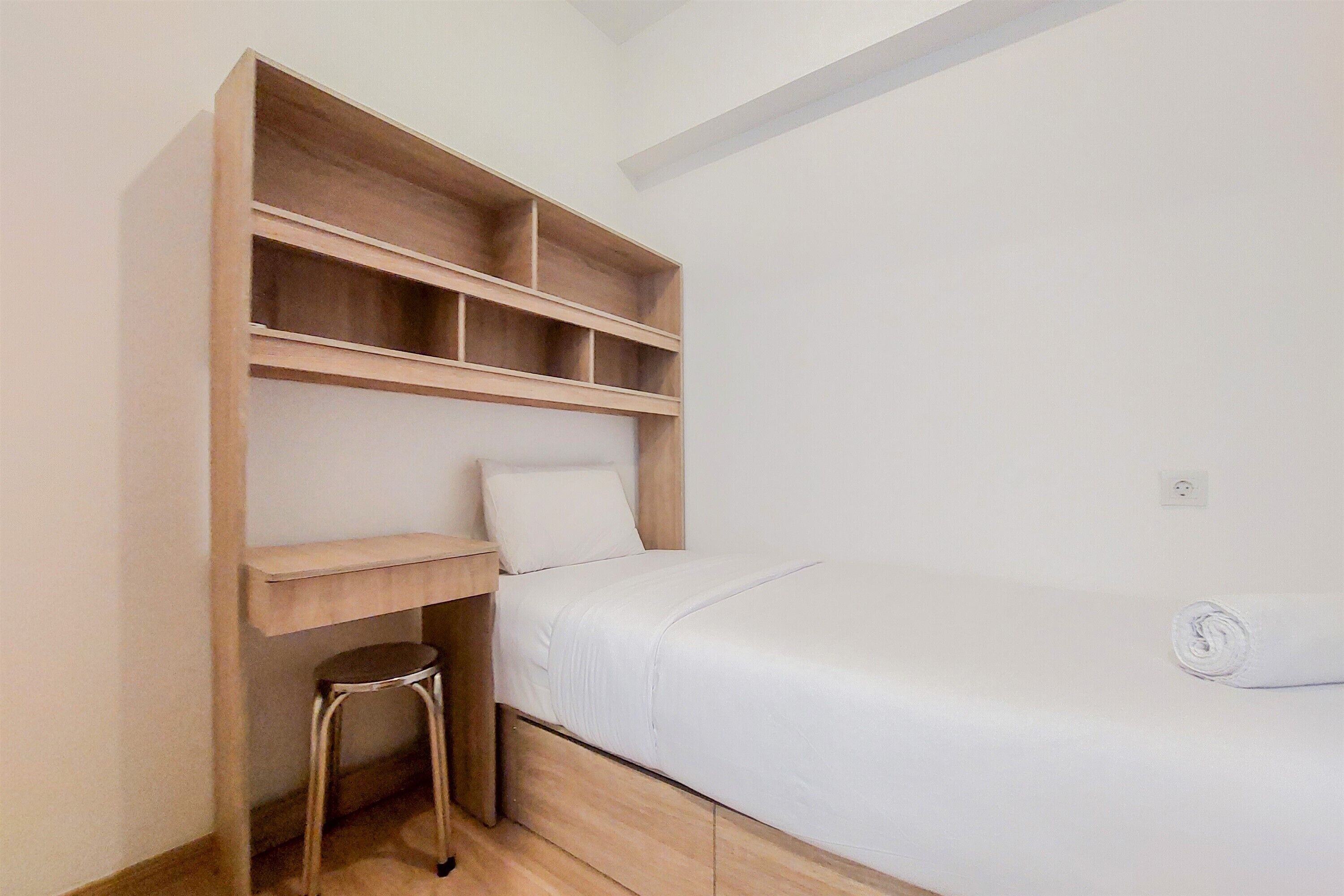 A small, neatly organized bedroom with a single bed, a wooden nightstand, a small stool, and built-in shelves above the bed.
