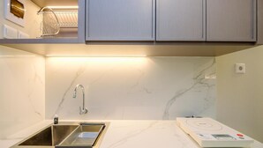 A modern kitchen with a built-in sink, a stainless steel faucet, a microwave, and a lighted countertop. - Modern And Comfy Studio At Tokyo Riverside Pik 2 Apartment (Teluknaga)